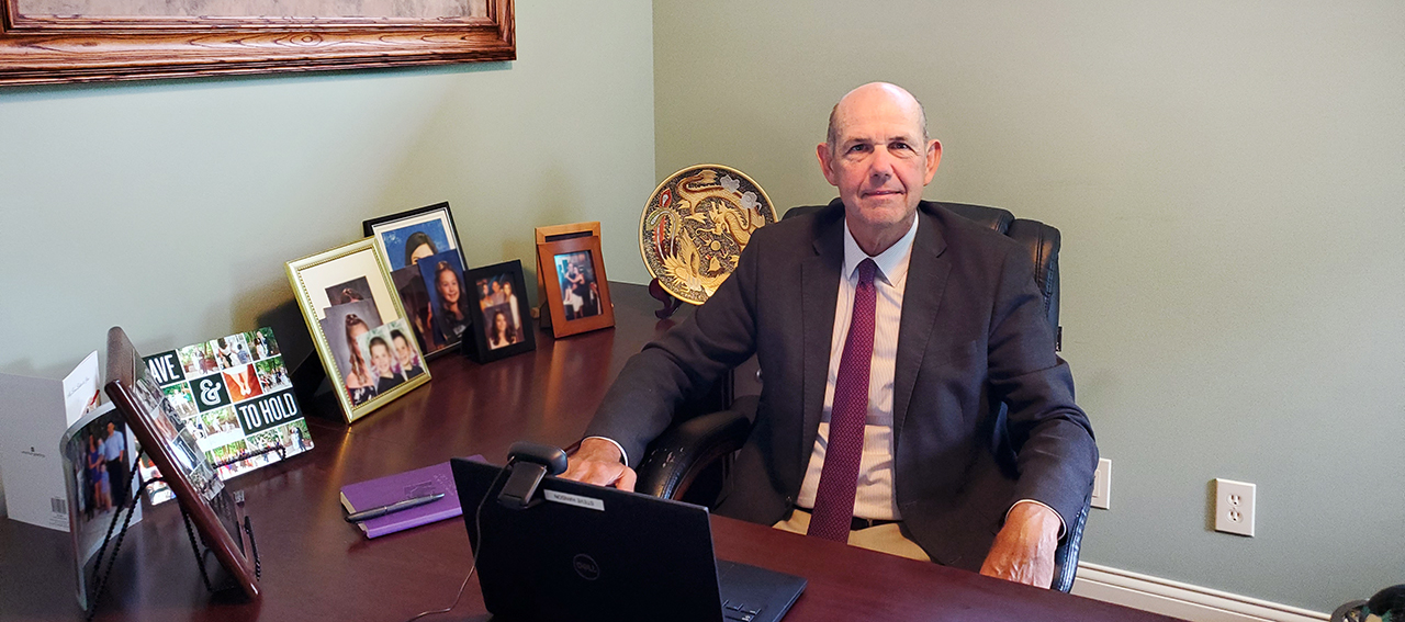 Steve Hanson sits at a large wooden desk with a laptop and photos of his family.