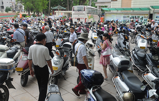 Men and women stand in crowd of mopeds