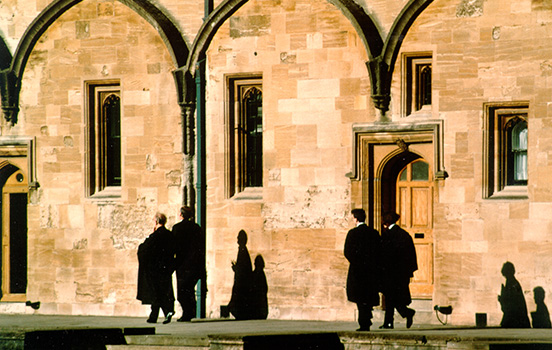Black-robed scholars walk outside stone building