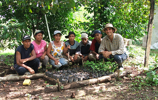 A peace corps volunteer with community members sitting around a small garden