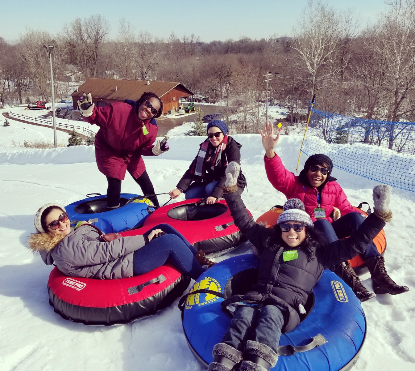 Five Humphrey Fellows smile at the camera sitting on large inflatable tubes on a snowy hill.